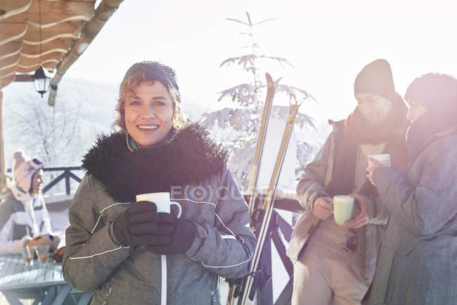 Портрет улыбающейся лыжницы пьющей кофе на палубе кабины с друзьями apres-ski — стоковое фото