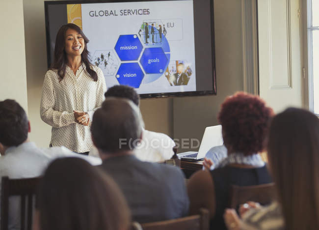 Smiling businesswoman leading business conference presentation at television screen — Stock Photo