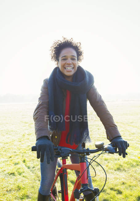 Портрет улыбающейся женщины на велосипеде в солнечной траве парка — стоковое фото
