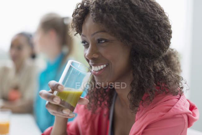 Mujer sonriente bebiendo batido verde saludable en la cafetería después del entrenamiento - foto de stock