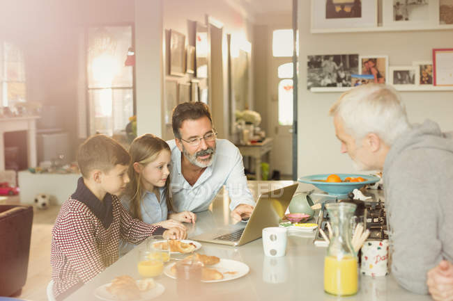 Hommes parents gays et les enfants à l'aide d'un ordinateur portable au comptoir de cuisine petit déjeuner — Photo de stock