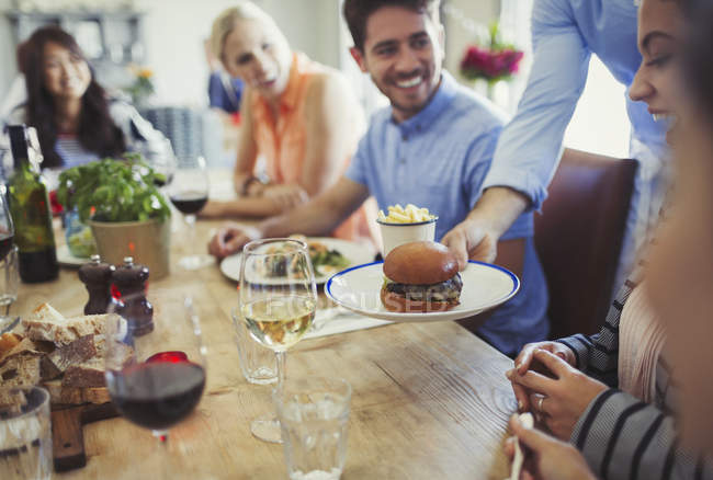Waiter serving slider hamburger to woman dining with friends at restaurant table — Stock Photo