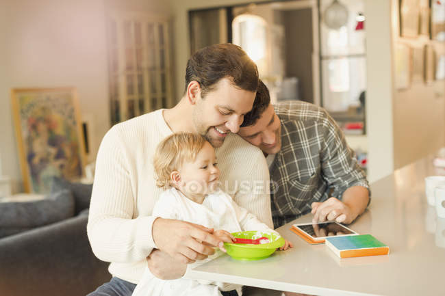 Чоловічі гей-батьки годують дитину сином і використовують цифровий планшет — стокове фото