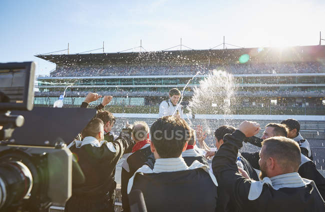 Formula one racing team spraying champagne on driver, celebrating victory on sports track — Stock Photo