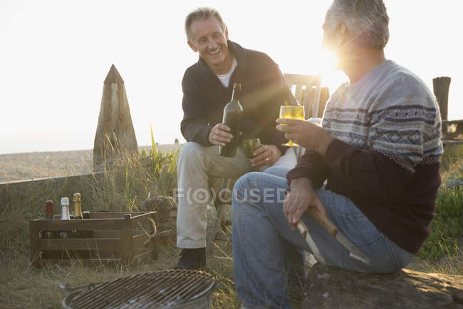 Senior men drinking wine and barbecuing on sunset beach — Stock Photo