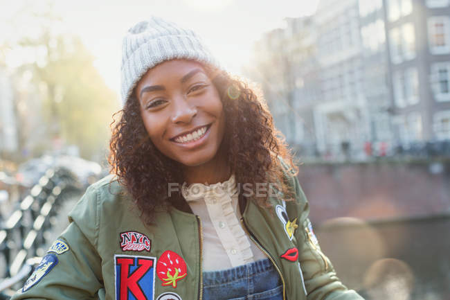 Retrato sonriente mujer joven en la soleada calle urbana de otoño - foto de stock