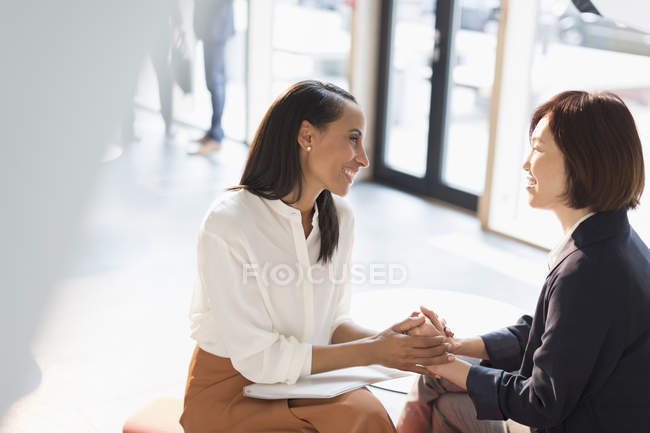 Усміхнені бізнес-леді тримають руки в сонячному офісному вестибюлі — стокове фото