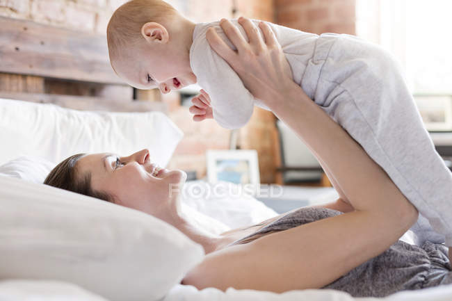 Sorridente madre che tiene la figlia del bambino sopra il letto — Foto stock