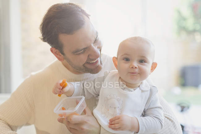 Portrait smiling, cute baby son and father eating carrots — Stock Photo