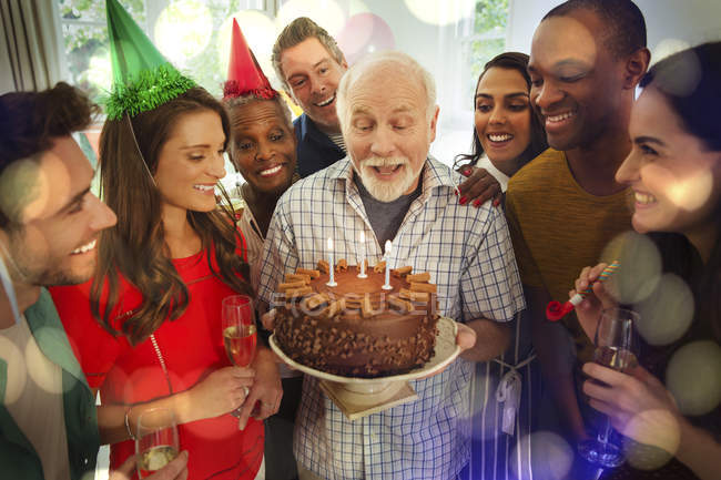 Багатоетнічна сім'я, яка спостерігає за старшим чоловіком, вибухає свічки на день народження на шоколадному торт — стокове фото