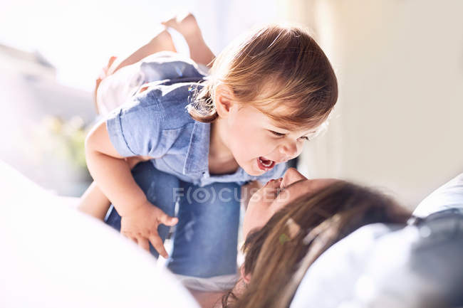 Juguetona madre sosteniendo riendo riendo bebé hijo de rodillas - foto de stock