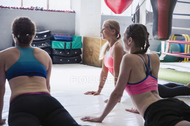 Las mujeres jóvenes que se estiran en la postura de yoga perro orientado hacia arriba en la clase de ejercicio - foto de stock