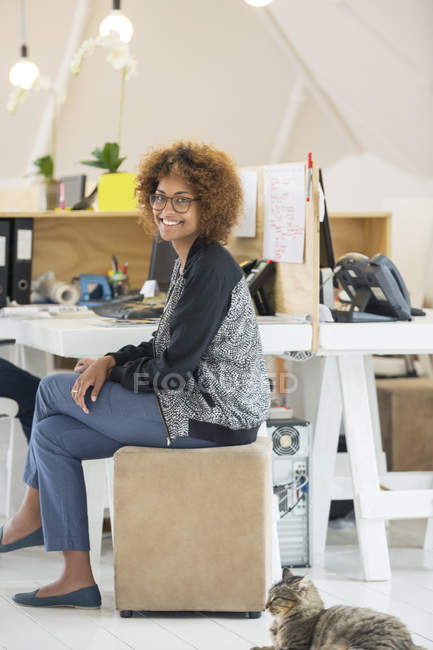 Молода усміхнена жінка сидить за столом в сучасному офісі — стокове фото