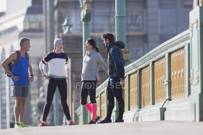Runners talking and stretching on sunny urban sidewalk — Stock Photo