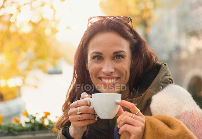 Portrait smiling woman drinking coffee at autumn sidewalk cafe — Stock Photo