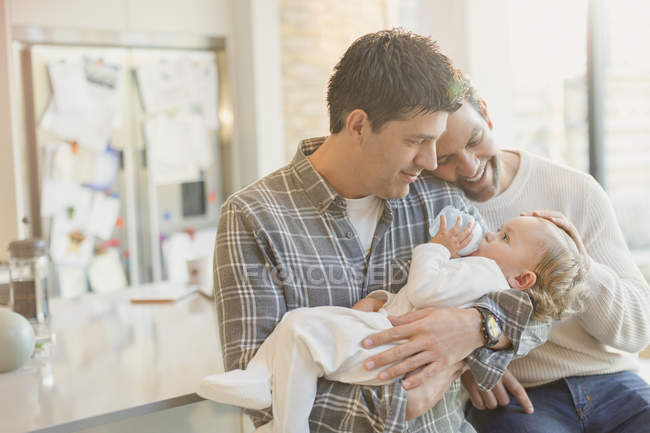 Afetuoso masculino gay pais segurando bebê filho com garrafa — Fotografia de Stock