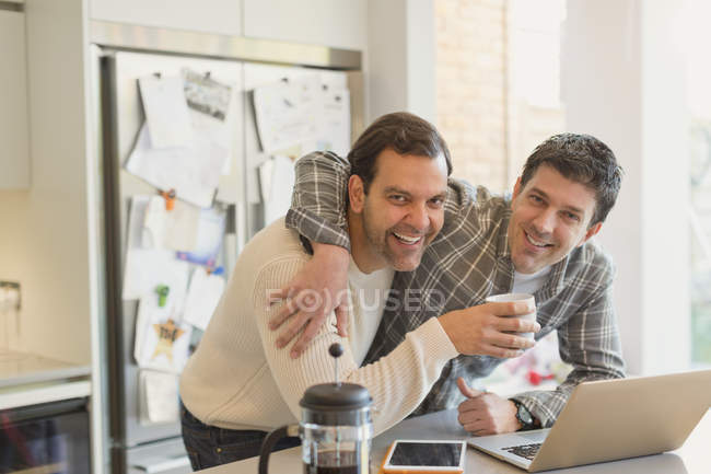 Portrait affectionate male gay couple drinking coffee and using laptop in kitchen — Stock Photo