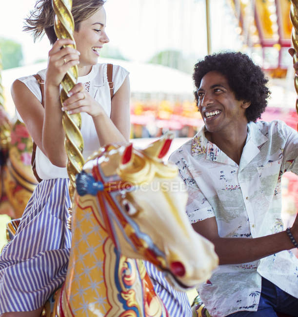 Jeune couple multiracial souriant sur le carrousel dans le parc d'attractions — Photo de stock