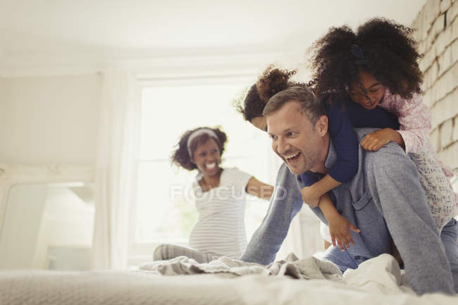 Multi-ethnic daughters tackling father on bed — Stock Photo