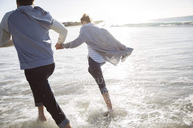 Jeune couple tenant la main et courant sur la plage — Photo de stock