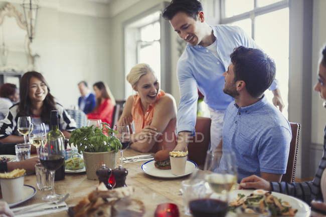 Camarero sirviendo comida a amigos cenando en la mesa del restaurante - foto de stock