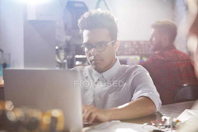 Diseñador masculino joven serio, centrado que trabaja en el ordenador portátil en el taller - foto de stock