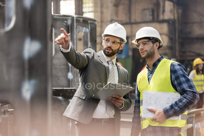 Manager and steel worker talking and looking away in factory — Stock Photo