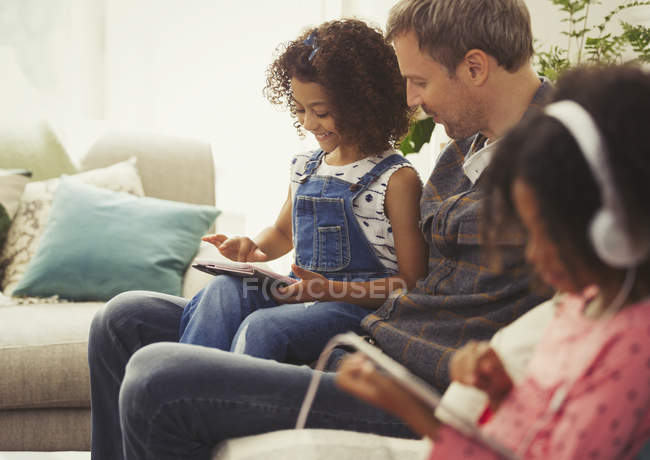 Padre e hija multiétnicos usando tableta digital en el sofá - foto de stock
