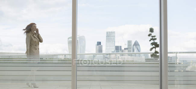 Businesswoman talking on cell phone on urban balcony with city view — Stock Photo