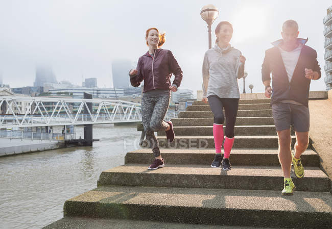 Runners running down steps along sunny urban waterfront — Stock Photo