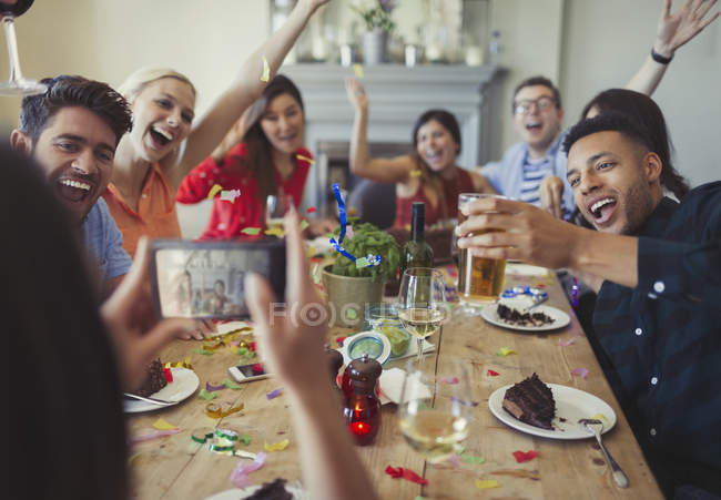 Femme avec appareil photo téléphone photographier amis ludiques jeter confettis à la table du restaurant — Photo de stock