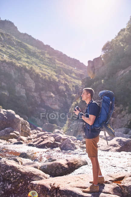 Молодий чоловік з рюкзаком пішохідний і фотографує сонячні, скелясті скелі з камерою — стокове фото