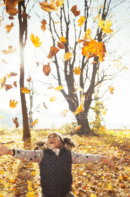 Ragazza giocosa gettando foglie in testa nel soleggiato parco autunnale — Foto stock