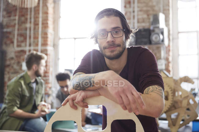Portrait confident male designer with tattoos leaning on prototype in workshop — Stock Photo