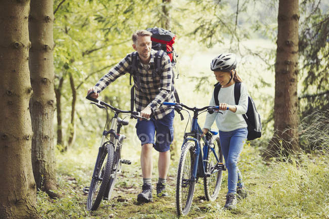 Отец и дочь с рюкзаками гуляют горные велосипеды в лесу — стоковое фото