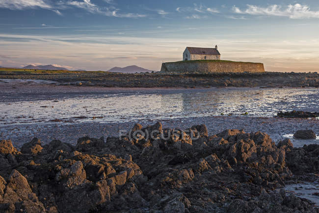 Iglesia tranquila de la isla medieval en la marea baja, Iglesia de St Cwyfans, Anglesey, Gales - foto de stock