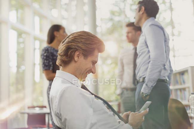 Smiling businessman texting with cell phone in office — Stock Photo