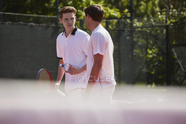 Male tennis players with tennis rackets talking on sunny tennis court — Stock Photo