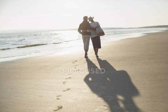 Ласковая зрелая пара, обнимающая и гуляющая по солнечному пляжу — стоковое фото