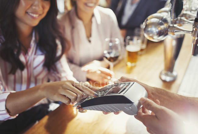 Femme payant barman en utilisant la machine de carte de crédit au bar — Photo de stock