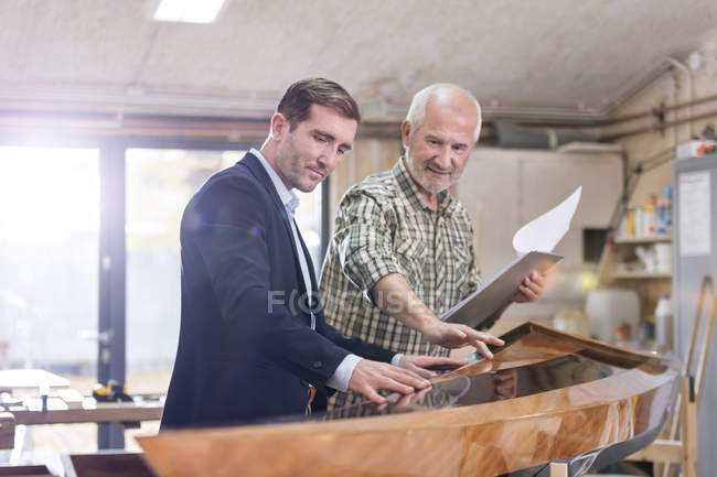 Carpintero masculino y cliente examinando madera kayak en taller - foto de stock