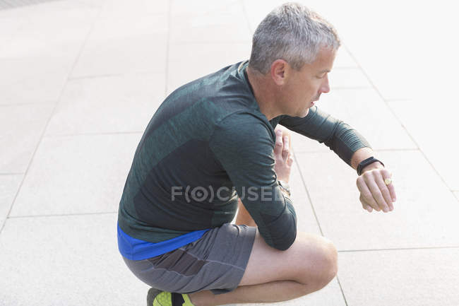 Corredor masculino descansando, agachado e verificando relógio de pulso — Fotografia de Stock