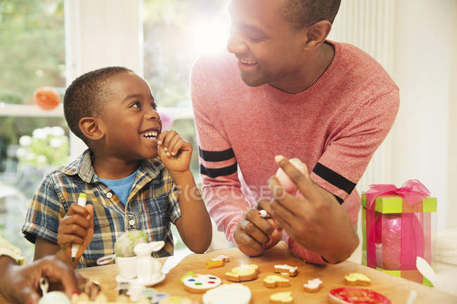 Sorrindo pai e filho decorando ovos de Páscoa e biscoitos — Fotografia de Stock