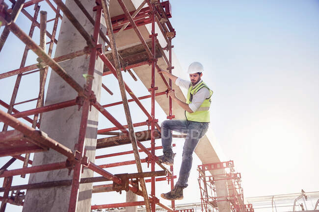 Trabajador de la construcción escalando barras de refuerzo en soleado sitio de construcción - foto de stock