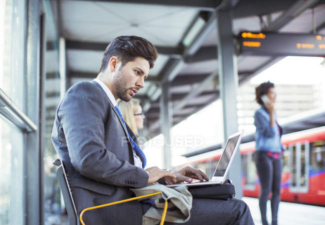 Businessman using laptop at train station — Stock Photo
