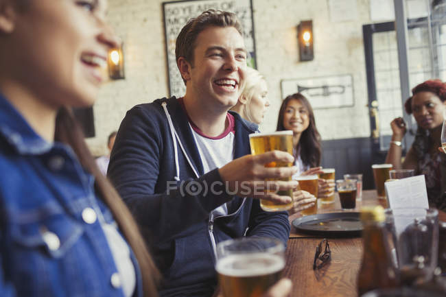 Uomo sorridente che beve birra con gli amici a tavola nel bar — Foto stock