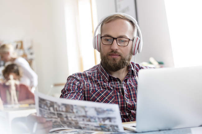 Design professional listening to music with headphones reviewing proofs at laptop — Stock Photo
