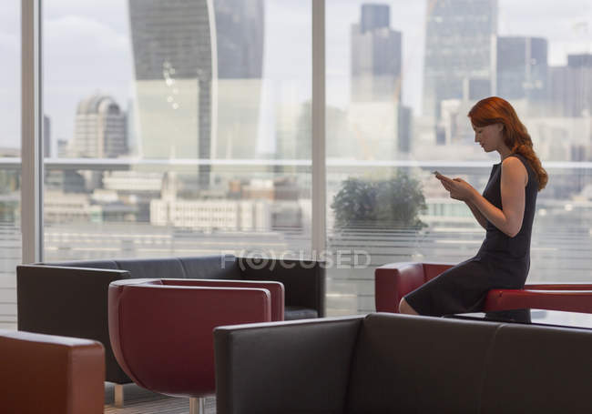 Mulher de negócios mensagens de texto com telefone celular no lounge urbano com vista para a cidade — Fotografia de Stock