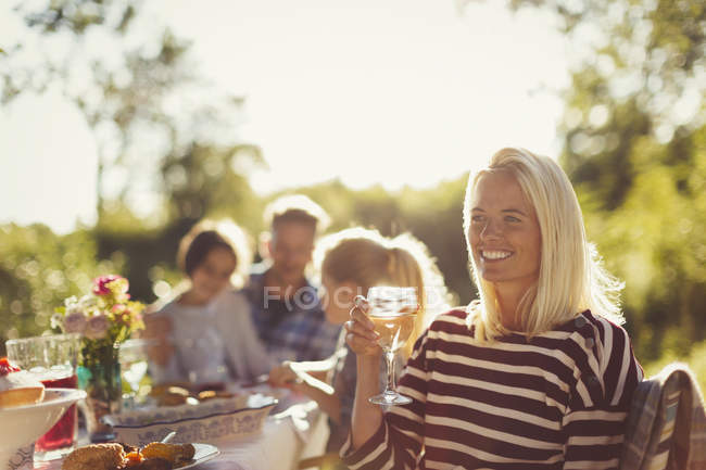 Donna sorridente bere vino al tavolo soleggiato patio festa giardino — Foto stock