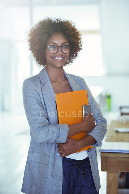Retrato del trabajador de oficina sonriente sosteniendo un archivo naranja y un teléfono inteligente - foto de stock